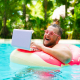 laughing Fat funny man in pink inflatable circle in pink glasses works on a laptop in a swimming pool.